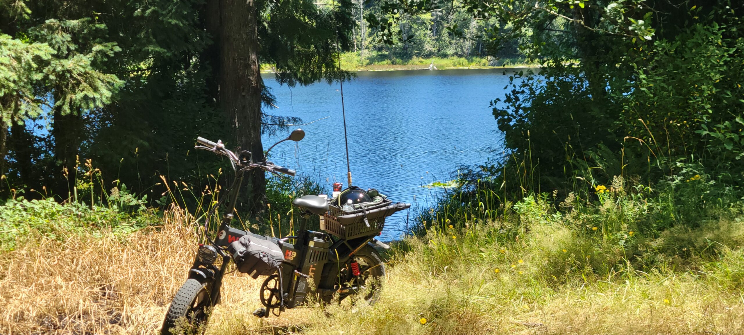 Wallke H9 all-wheel-drive ebike parked on a forest trail beside a small reflective lake, surrounded by lush evergreens in Washington State