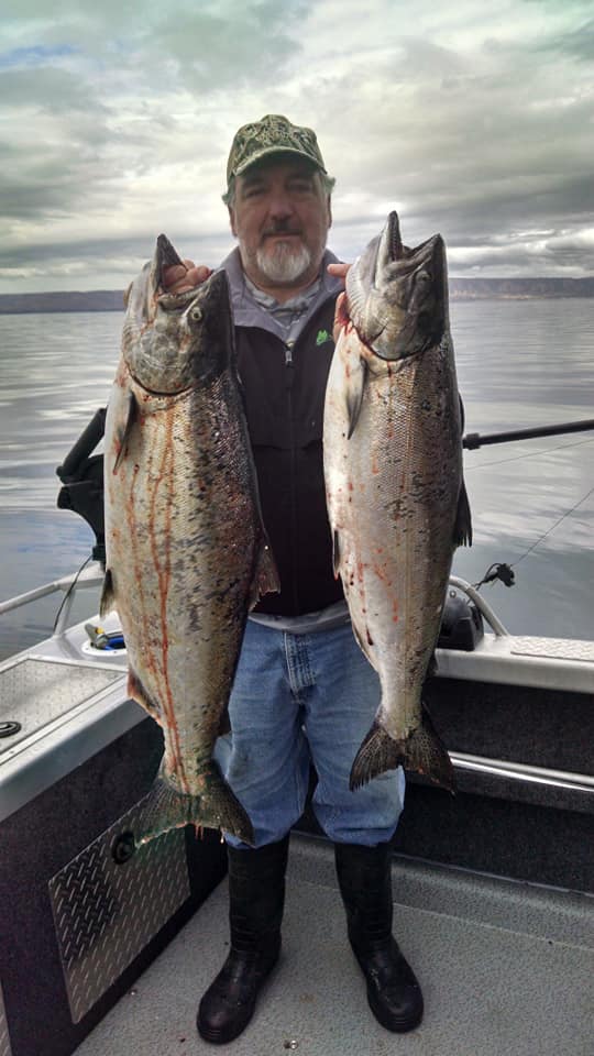 Richard from The Hunter Gatherer Society holding two large salmon in Alaska, celebrating a successful catch and the tradition of homemade pickled fish recipes.