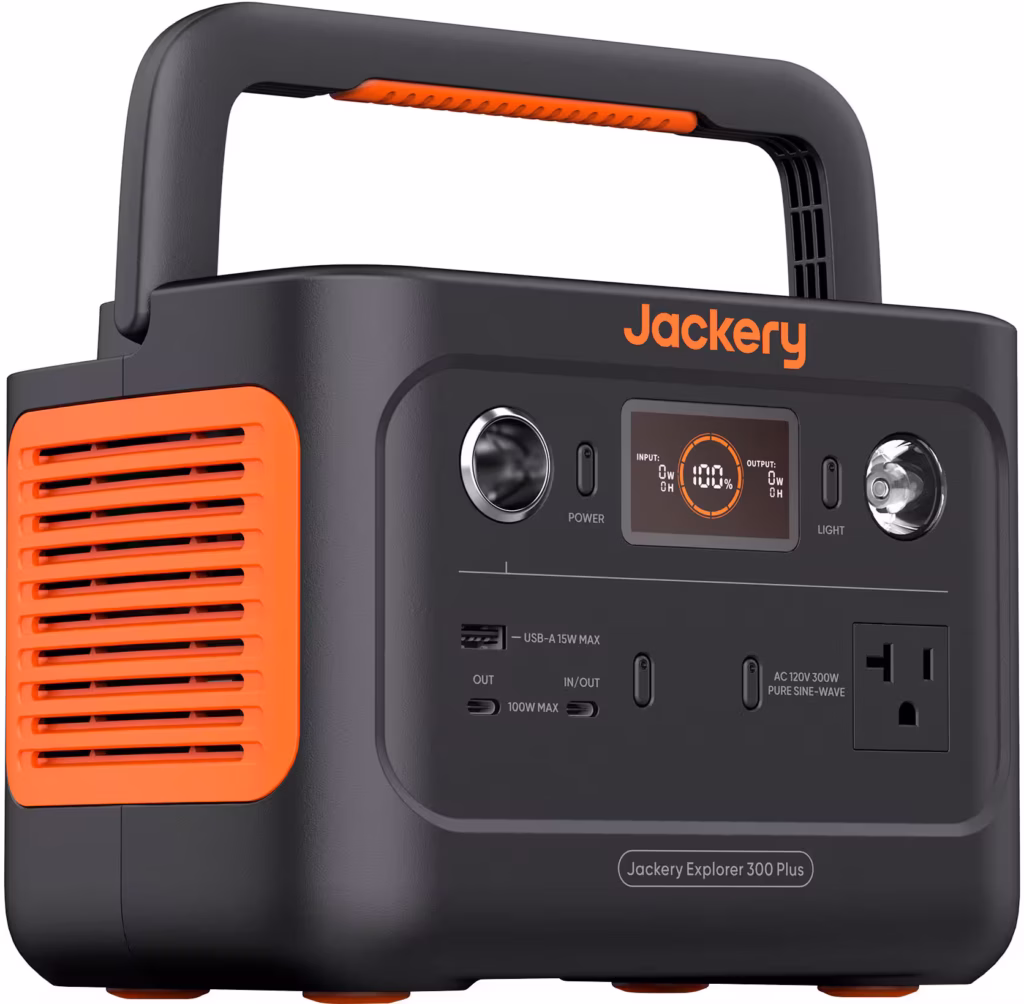 Jackery Explorer 300 Portable Power Station sitting on a wooden camp table, charging a phone and lantern beside a tent in the woods.