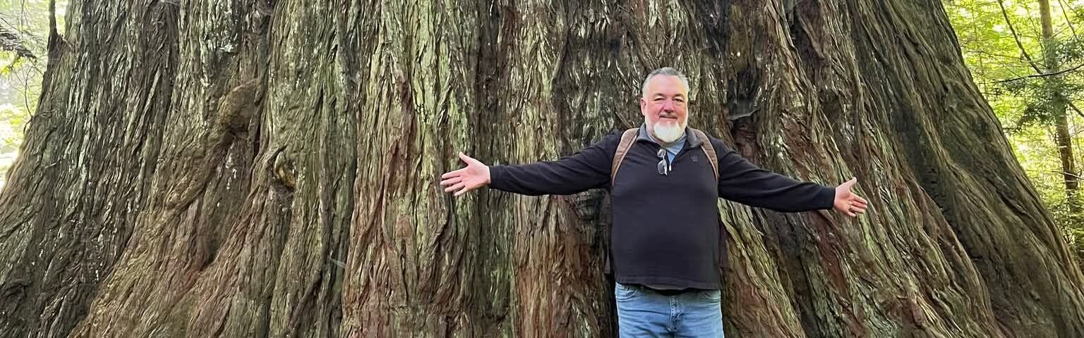 Standing at the base of a giant old-growth coast redwood along Big Tree Trail in Prairie Creek Redwoods State Park, California.