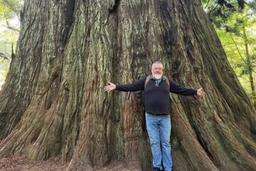 Standing at the base of a giant old-growth coast redwood along Big Tree Trail in Prairie Creek Redwoods State Park, California.